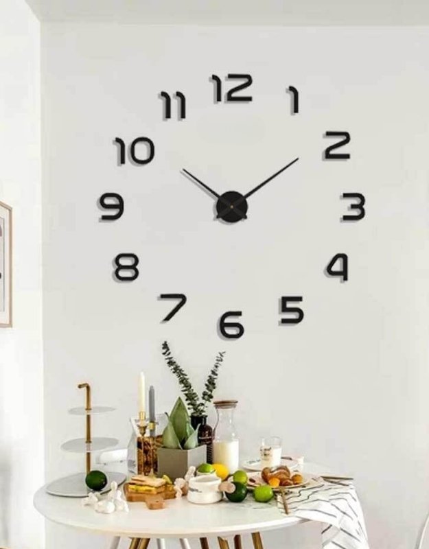 A black 3D wall clock sticker with self-adhesive numbers, displayed on a wall above a round table set with various items.